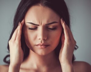 dunkelhaarige Frau mit Kopfschmerzen legt Hände an Schlafen