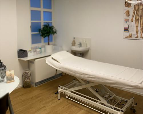 Behandlungsliege im hellen Behandlungsraum der Naturheilpraxis Munz mit Anatomie-Poster und Pflanze