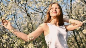 Junge Frau steht entspannt zwischen blühenden Frühlingszweigen