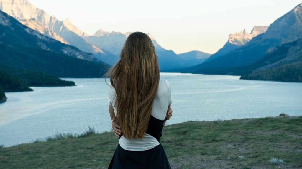 Frau steht vor einem Bergsee und blickt auf die umliegende Berglandschaft