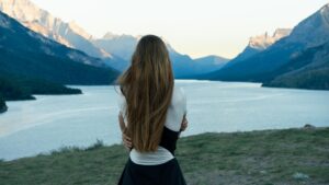 Frau steht vor einem Bergsee und blickt auf die umliegende Berglandschaft